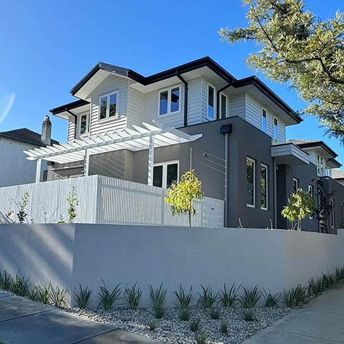 1-home-about-s1 Two-storey home with grey render, white pergola and a smooth rendered front wall