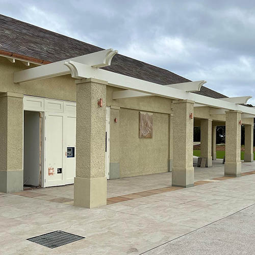 1-home-about-s3 Rendered pillars and doorways along a paved walkway under white pergola beams